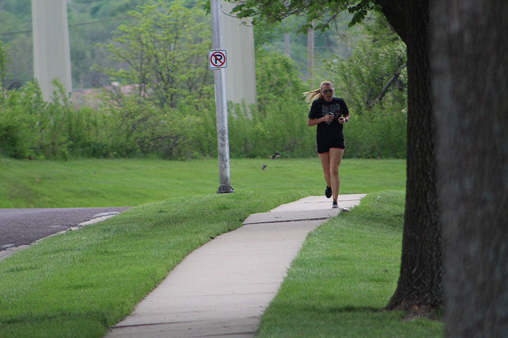 A woman runs down the sidewalk beside a tree